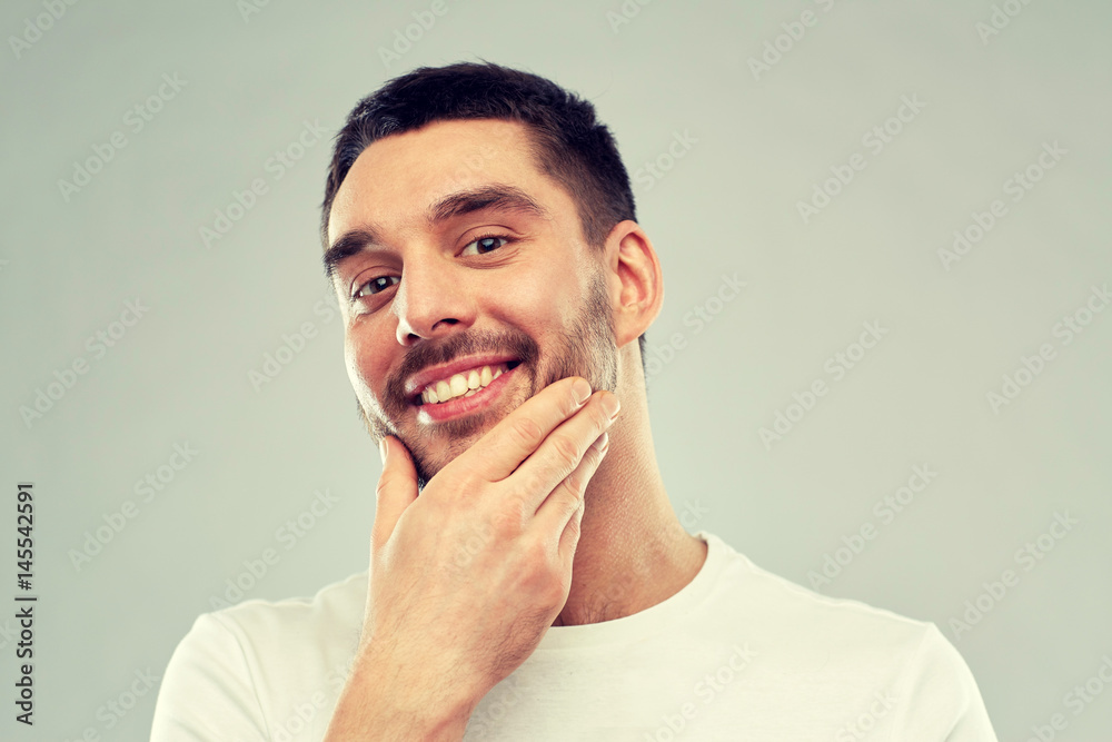 happy young man touching his face or beard happy young man touching his face or beard