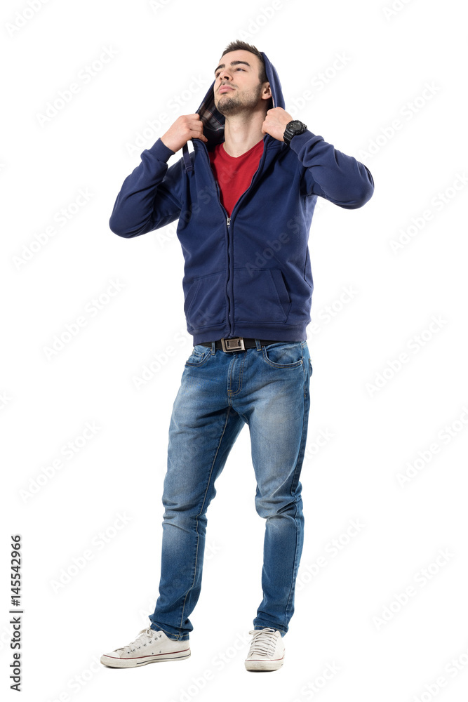 Cool handsome man putting on hoodie of blue sweatshirt looking up. Full body length portrait isolated over white studio background. Cool handsome man putting on hoodie of blue sweatshirt looking up. Full body length portrait isolated over white studio background.