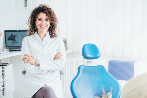Portrait of female dentist. She standing at her office and she has beautiful smile.
