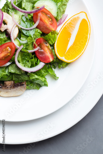 Salad of vegetables and champignons, lemon on white dishes.