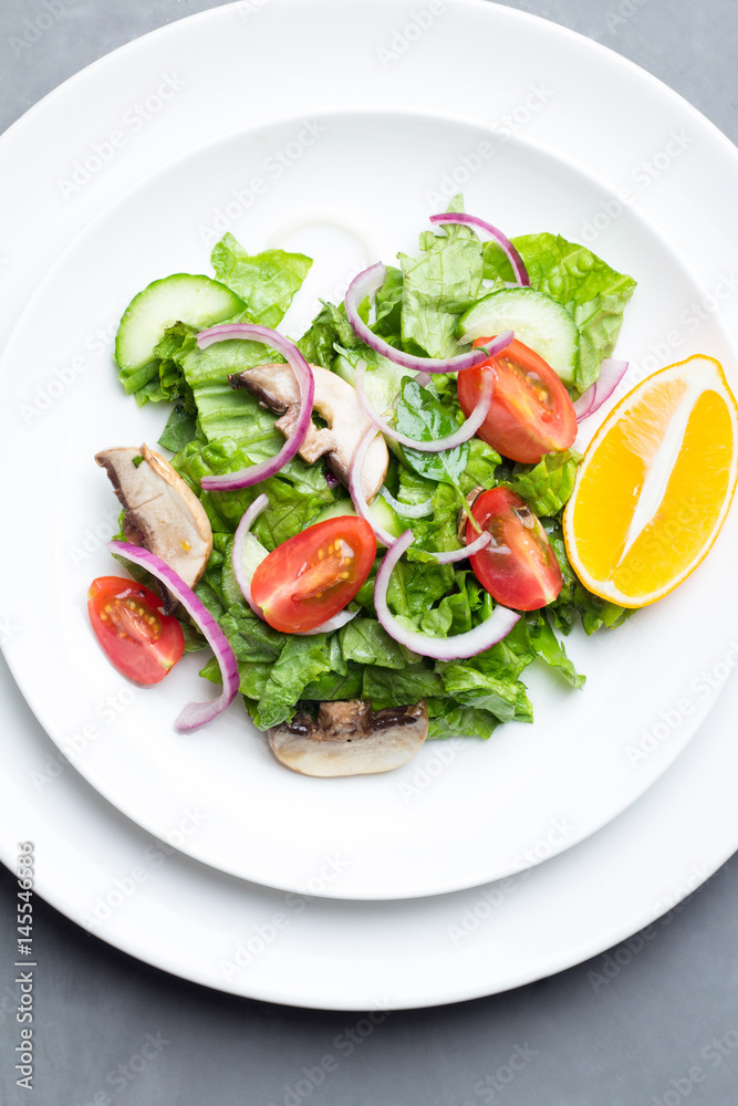 Salad of vegetables and champignons, lemon on white dishes top view.