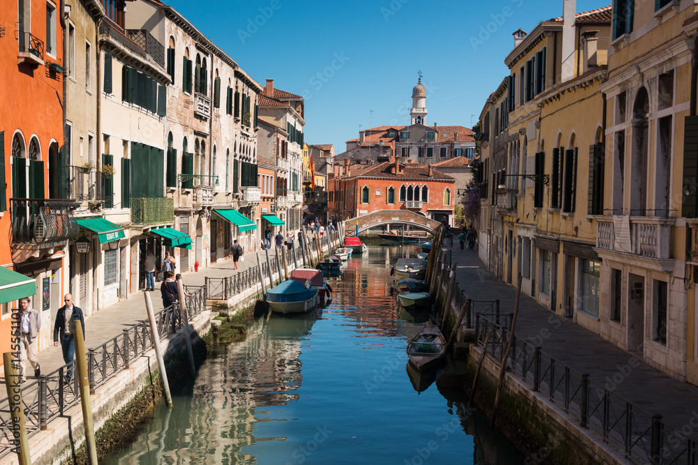 Narrow street with a canal, bridge, boats and tourists in Venice