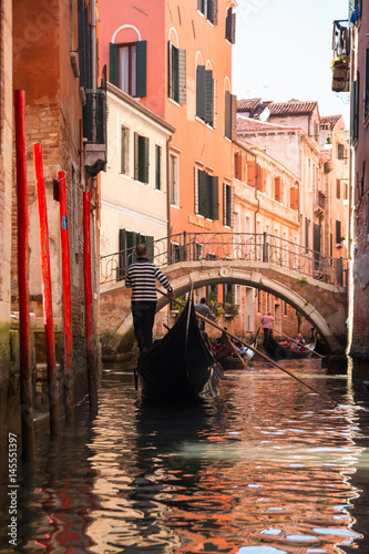 Gondola in narrow street with a canal, bridge and tourists in Venice