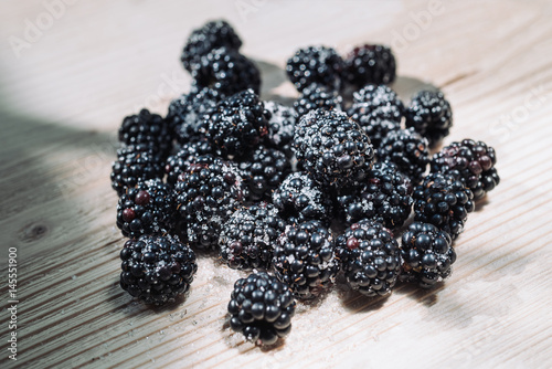 Ripe berries of dewberry on a wooden table. Healthy breakfast with vital vitamins. Ripe blackberry powdered with sugar. Sunlight shines through the frame of a window and illuminates berries