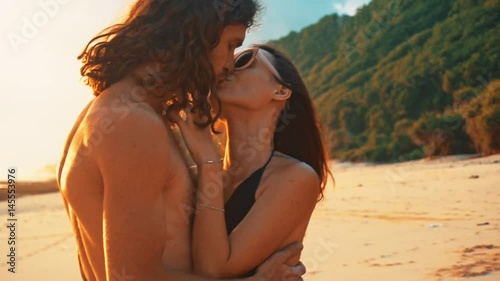Young happy couple hold each other and kiss on the beach at sunset on lonely beach, the magic hour