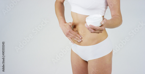 Young girl smears cream her beautiful, perfect body(waist), on a white background. Concept: vegetarian, diet, proper nutrition, spa procedures, fresh, fitness, bio products, body care, perfect skin.