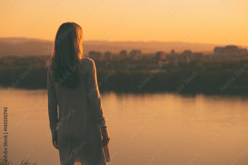 Lonely woman standing and looking at the sunset over the city.