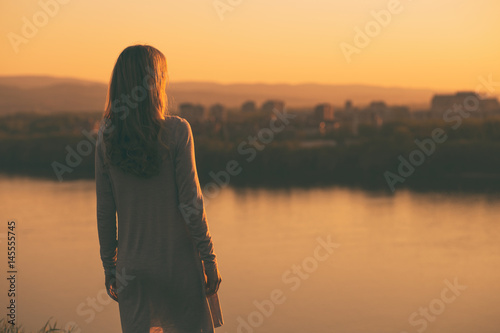 Lonely woman standing and looking at the sunset over the city. photo