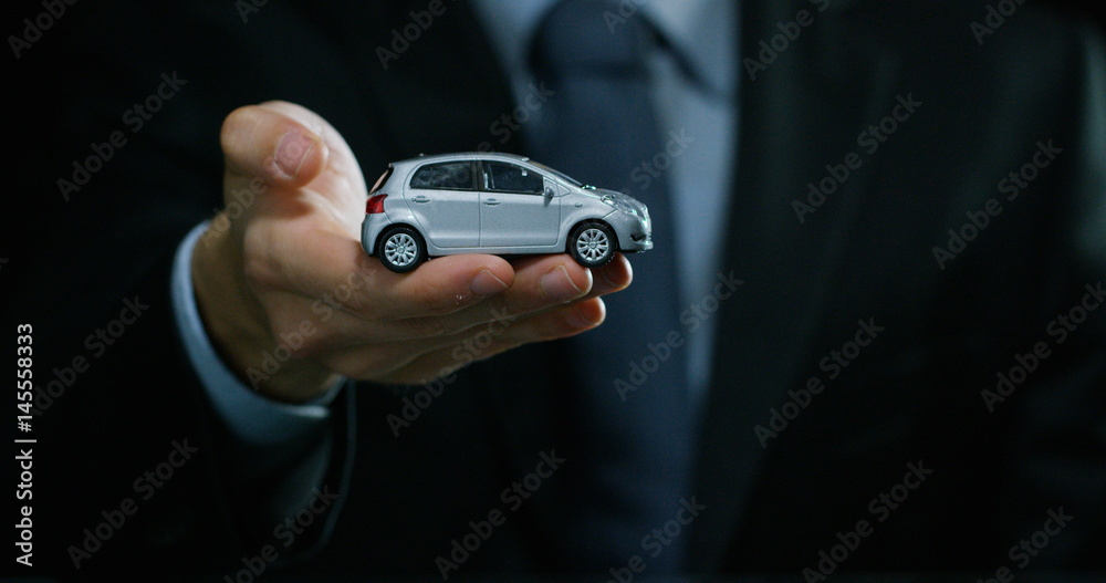 A man dressed in a suit and tie, shows a small auto. Concept: car insurance, mechanical, leasing, purchase new and used cars and public garages.