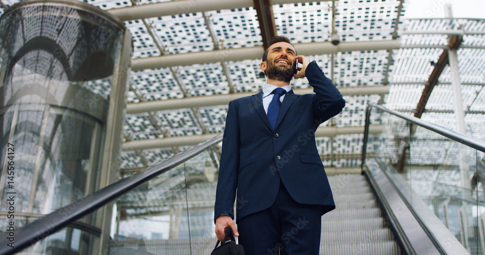 On escalators, a businessman answers the phone, send messages and smiles for the beautiful job news. Concept: technology, telephony, business trips, business.	