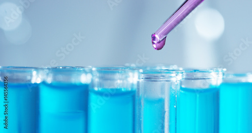 In a laboratory, a scientist with a pipette analyzes a colored liquid to extract the DNA and molecules in the test tubes. Concept: research, biochemistry, nature, pharmaceutical medicine 