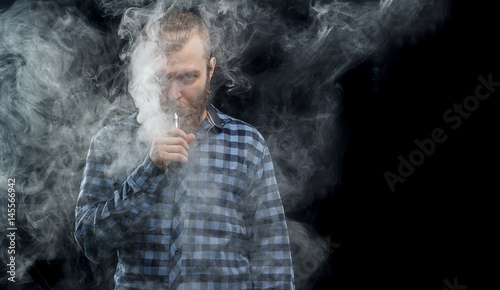 Vaping man holding a mod. A cloud of vapor. Black background. Studio shooting.