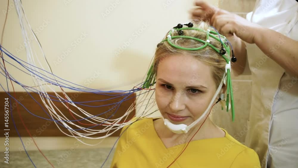 Electroencephalographic examination. The female doctor preparing young blond-haired woman for brain scan in the hospital. HD
