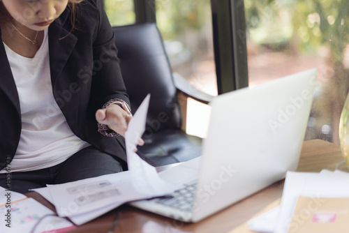Asian female accountant or banker is busy working with laptop, smart phone and document in home office in selective focus. Concept : Busywork © ichz