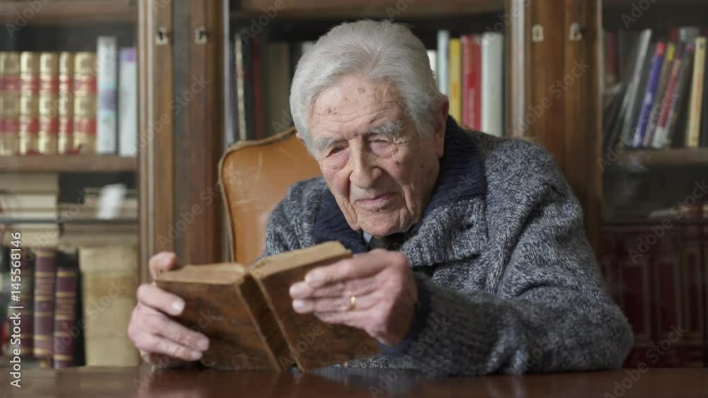 Very old man sitting at desk reading a book,portrait