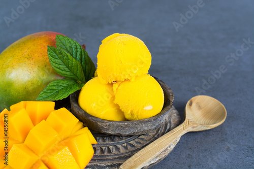 Mango ice cream sorbet with mint leaves and mango fruit in black stone bowl on grey textured backgund photo