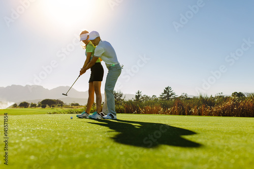 Man teaching woman to play golf on field
