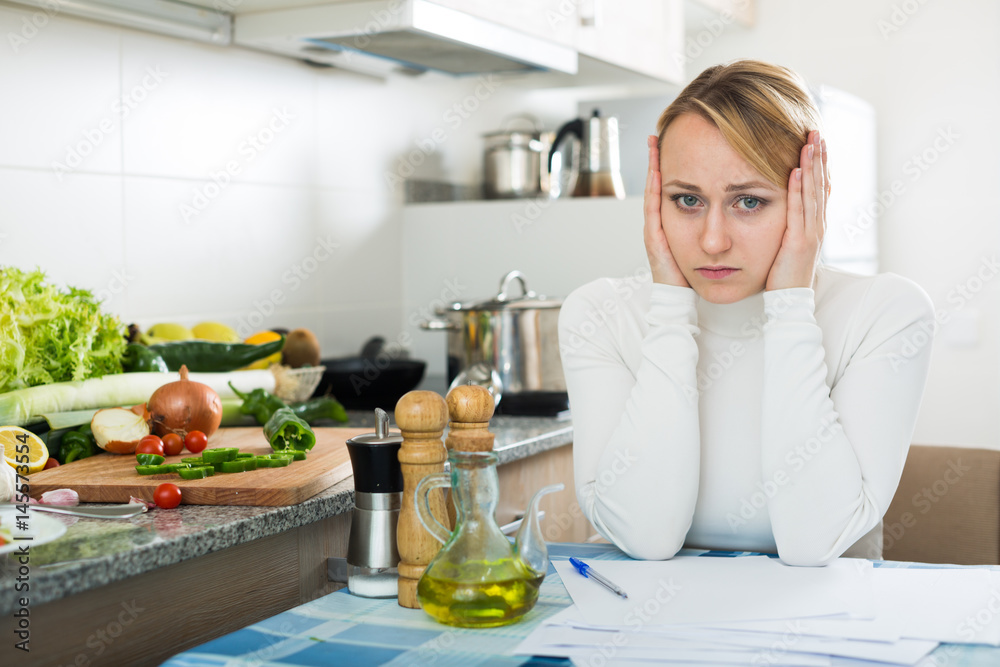 Upset woman calculating budget in kitchen