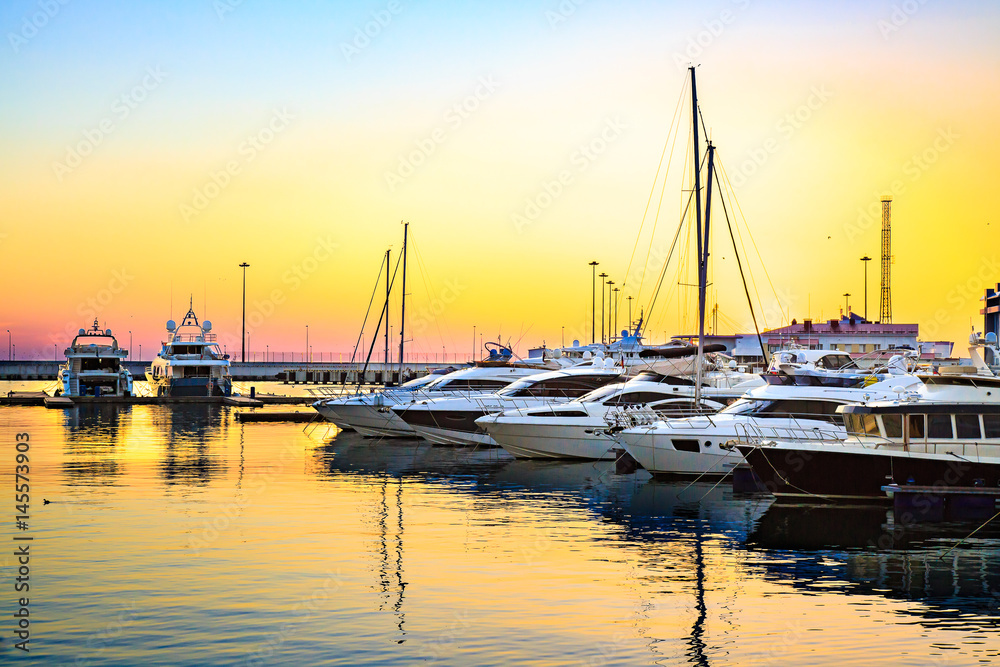 Luxury yachts docked in sea port at colorful sunset. Marine parking of modern motor boats.