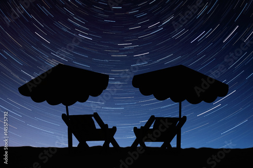 Silhouettes of sun loungers with umbrellas on the background of star tracks
