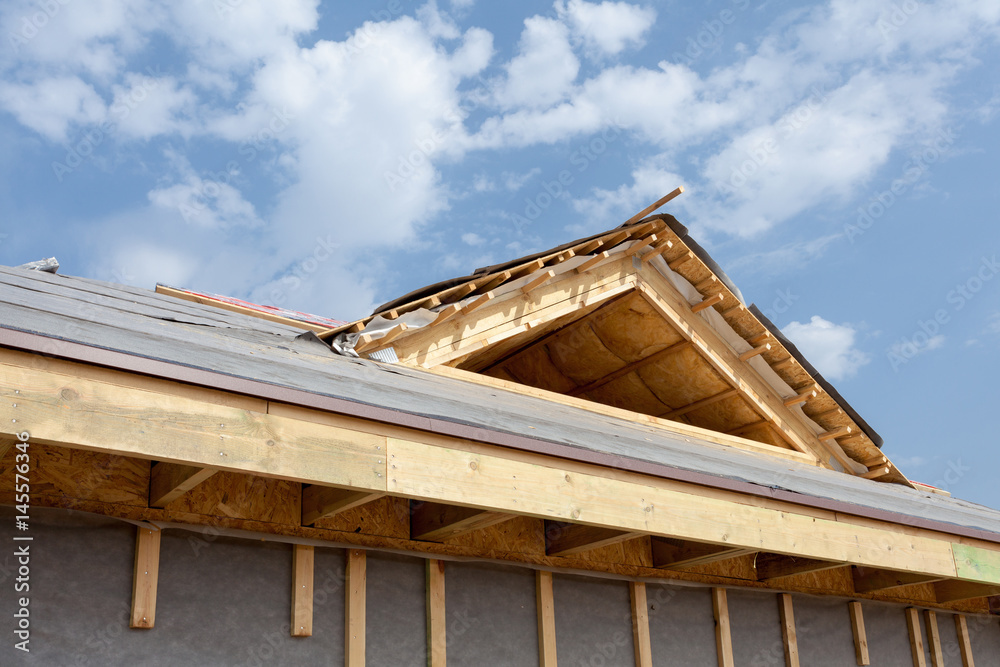 New frame house under construction. Roof with asphalt shingles, chimney and insulation material in attic