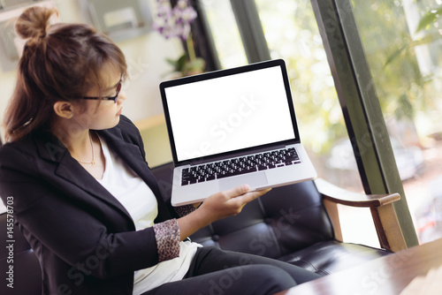 Asian woman using laptop and presenting with blank screen laptop in selective focus.