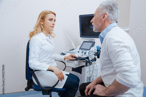 Attractive sonographer having conversation with aged patient at work