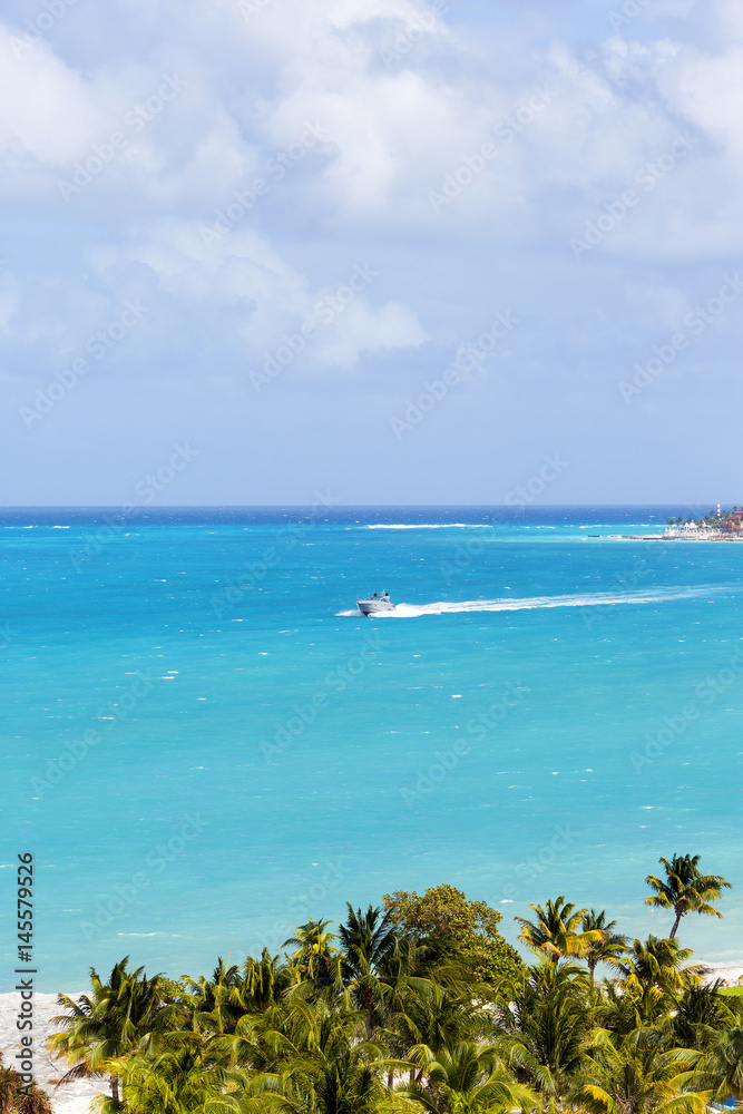 Aerial view to the sea. Turquoise water of the Caribbean sea. Big yacht is cruising from the hotel zone. Palm trees in front. View to paradise.