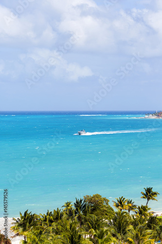 Aerial view to the sea. Turquoise water of the Caribbean sea. Big yacht is cruising from the hotel zone. Palm trees in front. View to paradise.