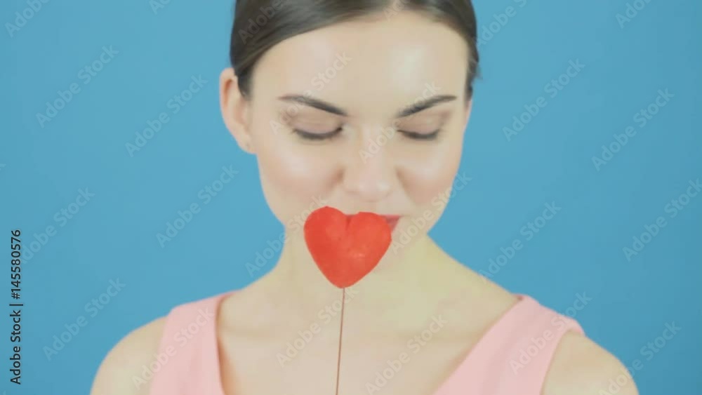Amazing Brunette with Little Red Heart in Hand Posing and Making Air Kiss on Blue Background in Studio. Amazing Brunette with Little Red Heart in Hand Posing and Making Air Kiss on Blue Background in Studio.