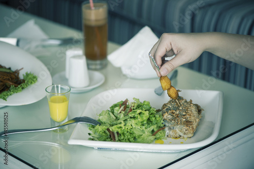 Fish with a salad in a plate is servered on a table with a glass of carrot juice. The female is having lunch. photo