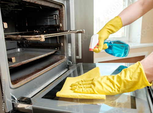 Man with bottle of spray and rag cleaning oven