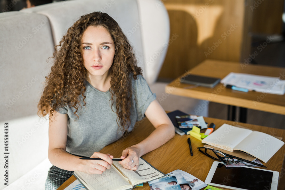 Fototapeta premium Young serious businesswoman looking at camera while planning her work