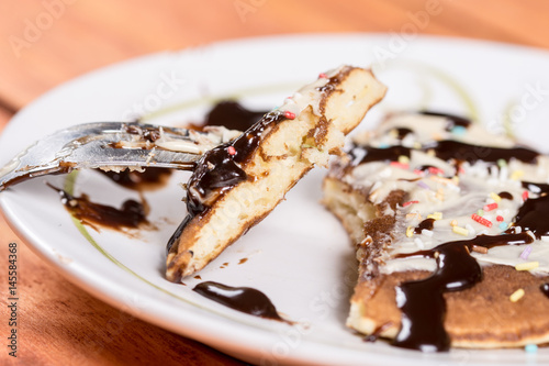 Slice of american pancake topped with chocolate cream and sprinkles on the fork closeup macro