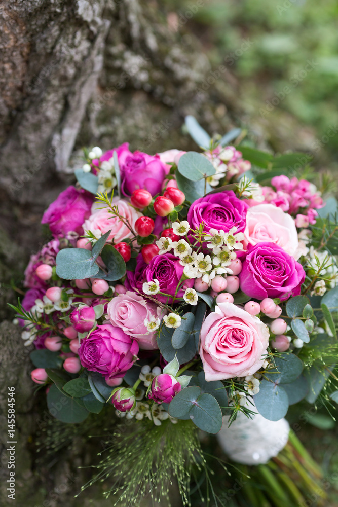 Close-up of pink roses wedding bouquet placed outdoors next to a tree trunk