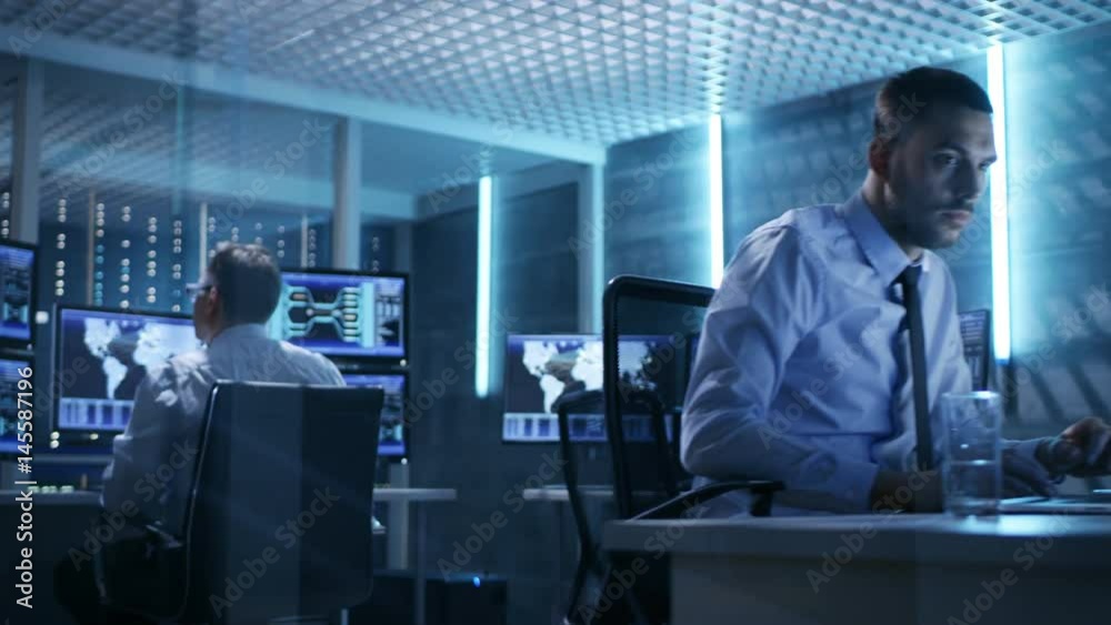 Two Technical Engineers at Sitting at Their Workplaces With Multiple Displays. They're in Monitoring Room with Servers.  Shot on RED EPIC-W 8K Helium Cinema Camera.