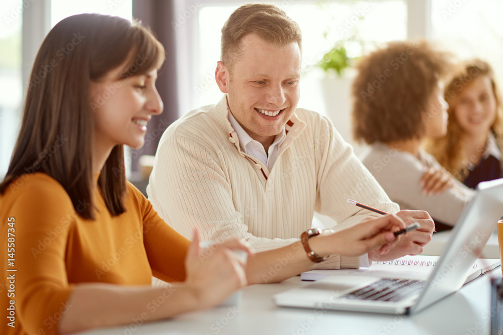 Young happy people discussing business standing at the whiteboard in modern light office, beautiful woman sitting at the table at forefront Young happy people discussing business standing at the whiteboard in modern light office, beautiful woman sitting at the table at forefront