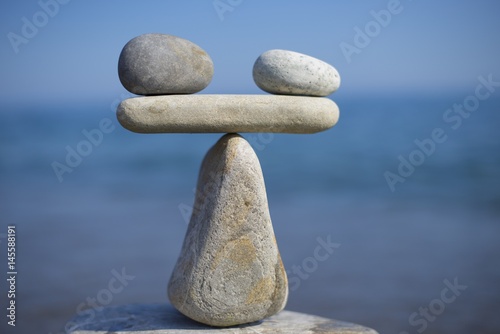 Balance of stones. To weight pros and cons. Balancing stones on the top of boulder. Close up. Balance of stones on a blue sky background with a copy space.Scales.Stones balance, sustainability. Scale
