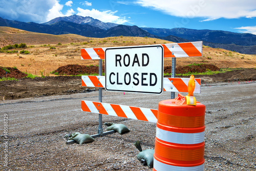 Road closed sign with cone on dirt road photo