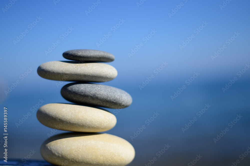 Zen spa stones with blue water and sky. Balanced stones background, copy space. Spa symbol. Balancing stones. Symbol of stability. Tranquil, relaxation and health life. Stones balance. Sustainability.