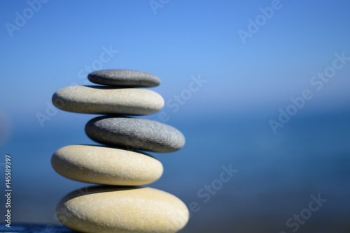 Zen spa stones with blue water and sky. Balanced stones background  copy space. Spa symbol. Balancing stones. Symbol of stability. Tranquil  relaxation and health life. Stones balance. Sustainability.