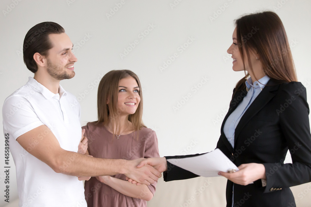 Portrait of happy smiling couple and real estate broker shaking hands, young family meeting with banker to discuss mortgage loan, female advisor handshaking clients, visiting notary office Portrait of happy smiling couple and real estate broker shaking hands, young family meeting with banker to discuss mortgage loan, female advisor handshaking clients, visiting notary office