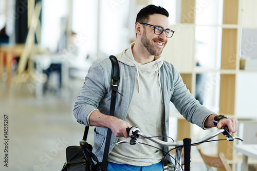 Portrait of casual contemporary business man taking bicycle to work in modern creative office