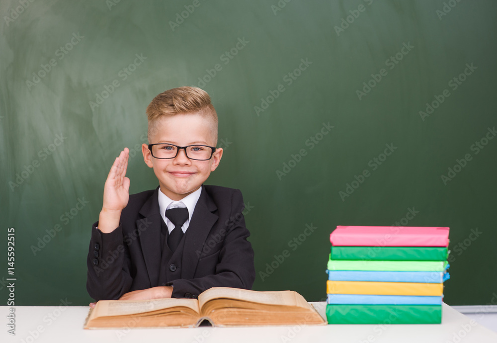 Young boy in a suit raising hand knowing the answer to the question Young boy in a suit raising hand knowing the answer to the question