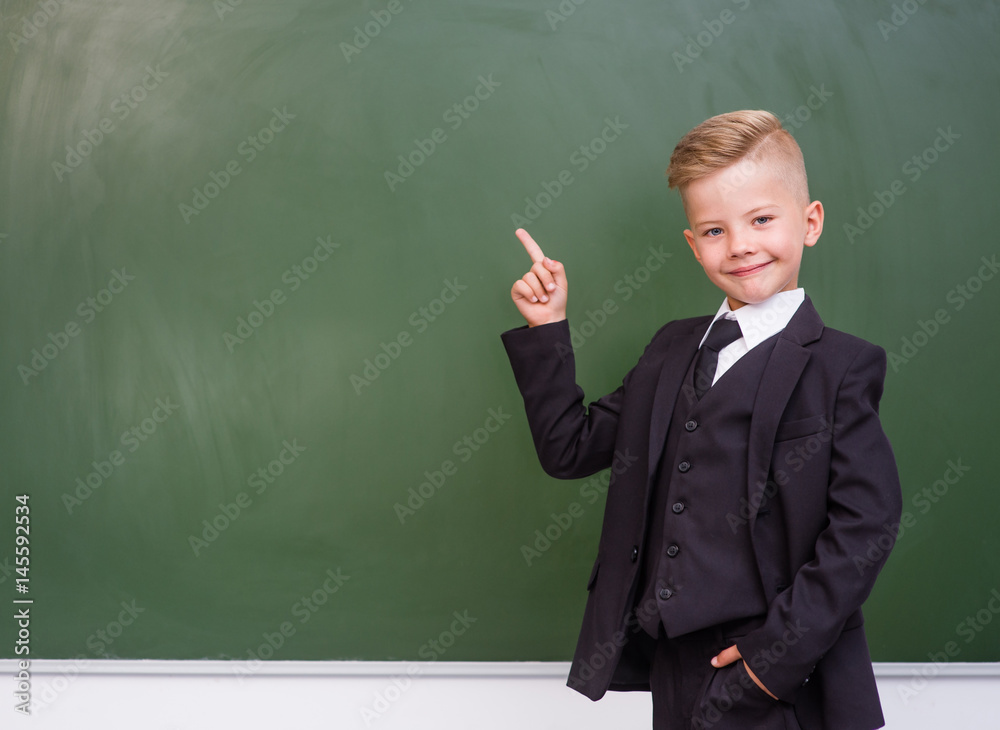 Boy in a suit points on empty green chalkboard Boy in a suit points on empty green chalkboard