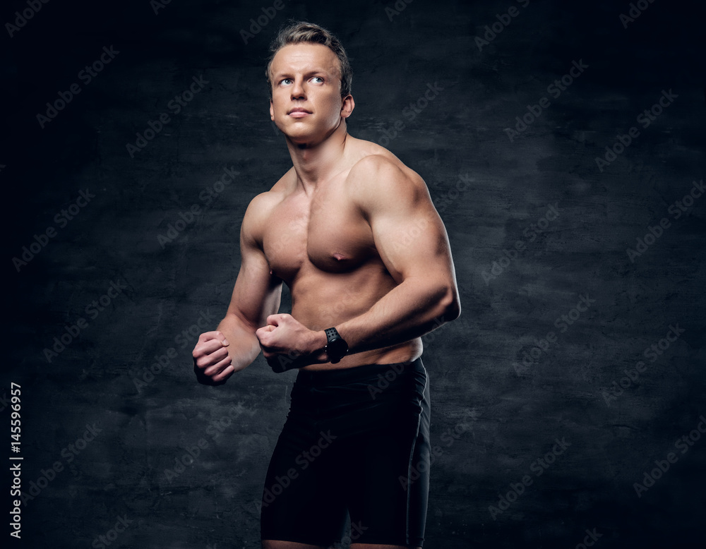 Portrait of shirtless athletic male with crossed arms over dark grey background.