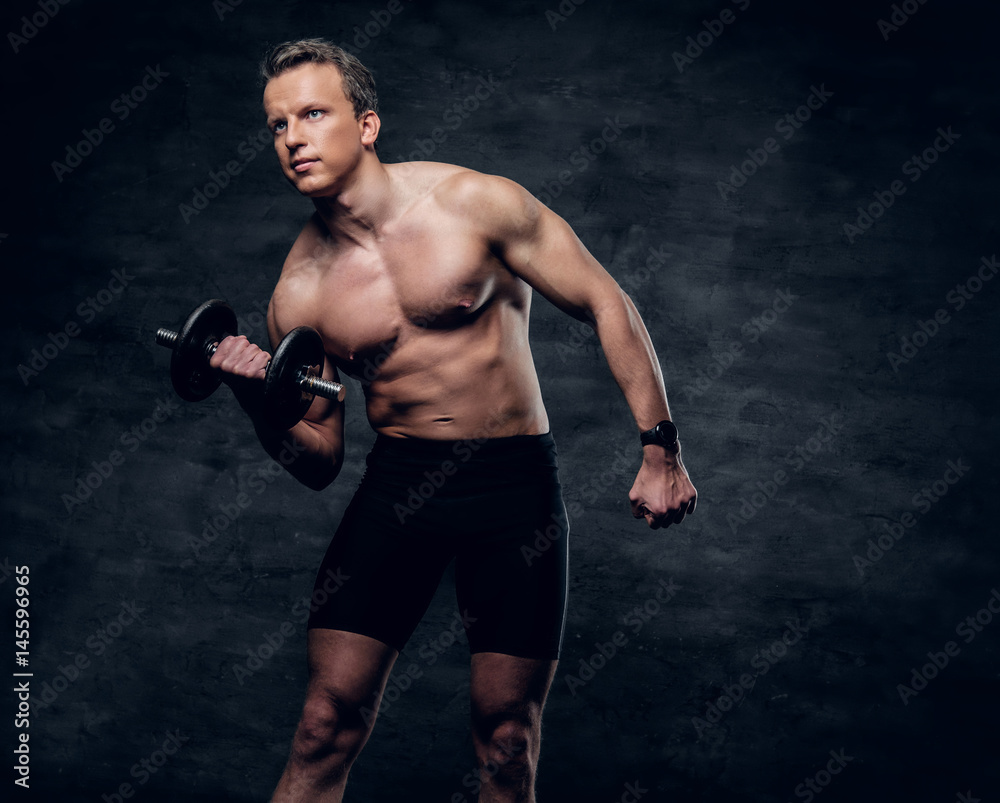 Portrait of shirtless athletic male doing a biceps workout with dumbbell.