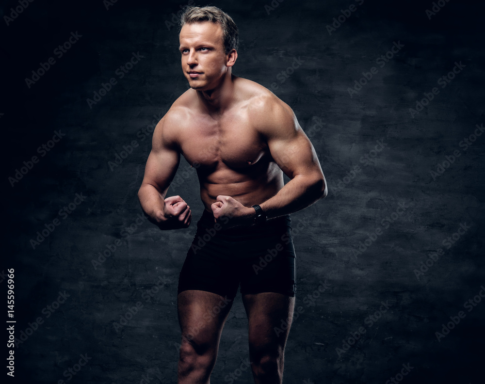 Portrait of shirtless athletic male with crossed arms over dark grey background.