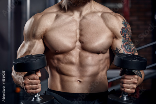 Athlete muscular bodybuilder with dumbbells.