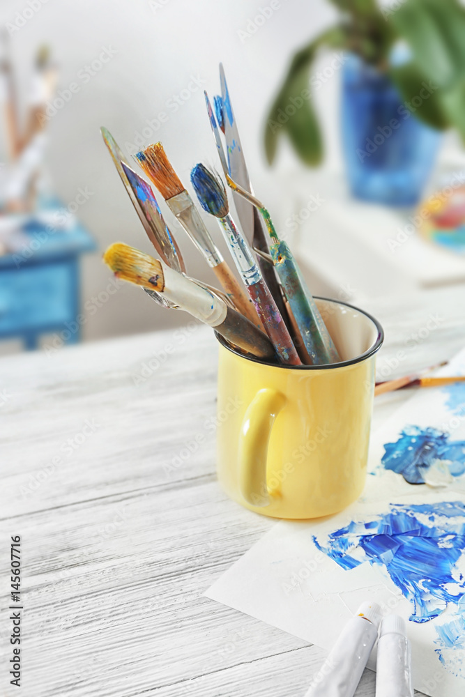 Metal mug with brushes and palette knives on painter's working table